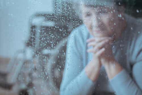 Mujer mayor mirando la lluvia por la ventana
