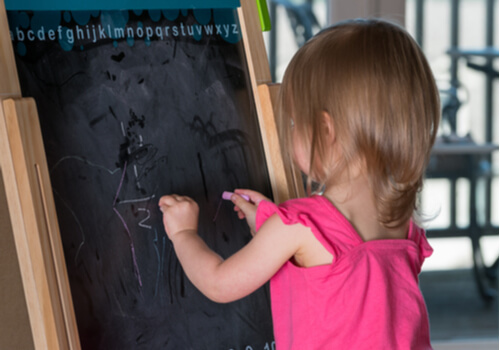 Niña escribiendo en una pizarra con las dos manos