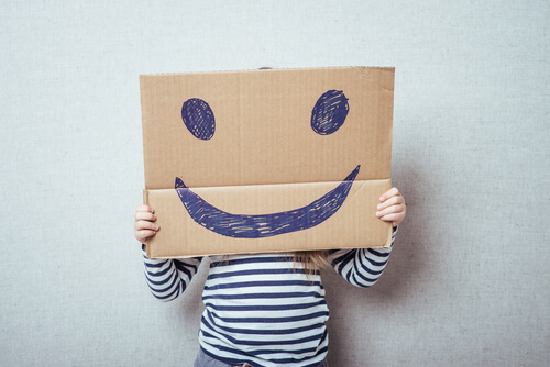 Niño con un cartón en el que hay dibujada una cara feliz