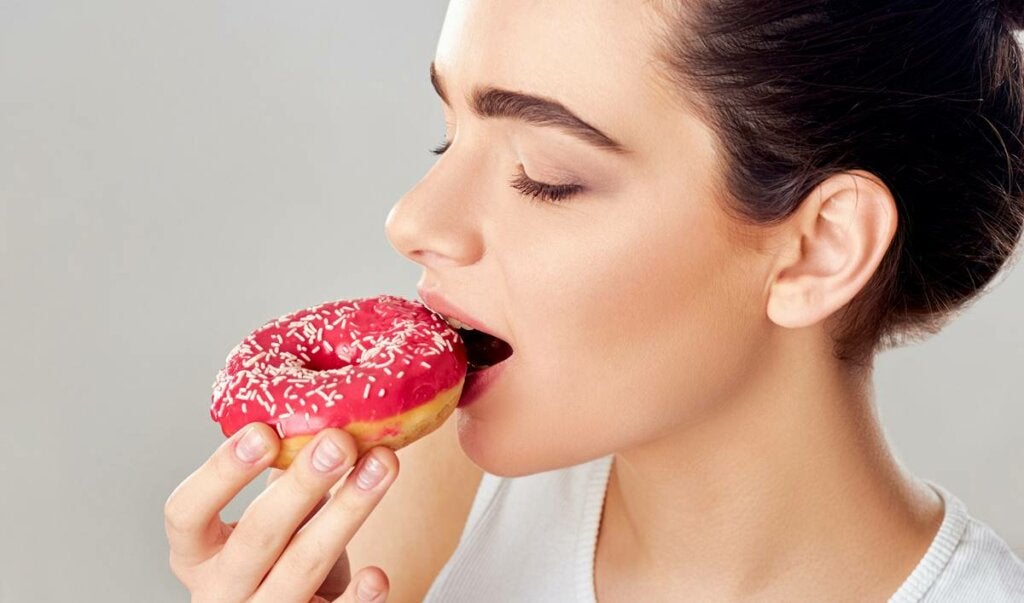 Mujer comiendo donut pensando en ¿Por qué tengo hambre a todas horas?