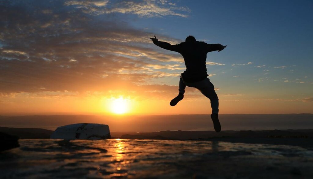 Hombre saltando feliz por tomar la iniciativa en una playa al amanecer