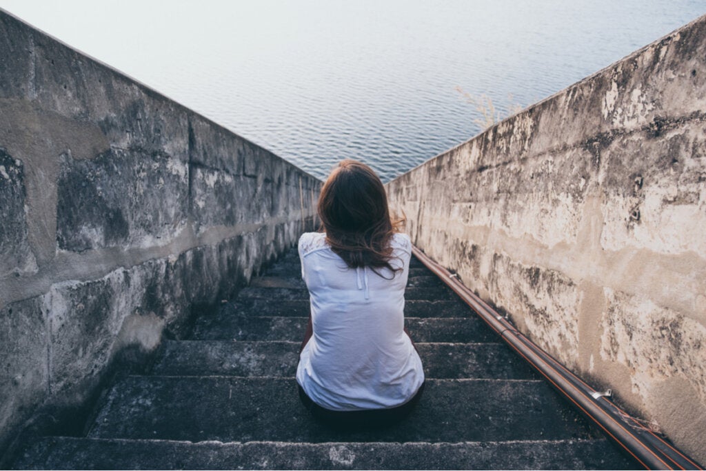 Mujer sentada en una escalera mirando el mar