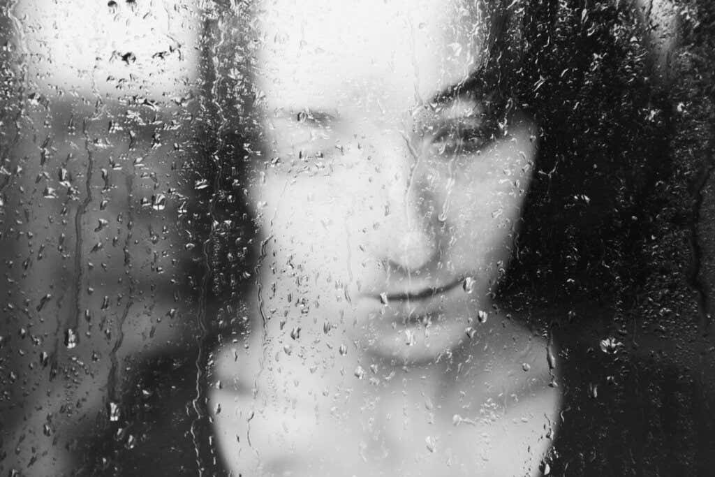 Mujer triste mirando la lluvia por la ventana