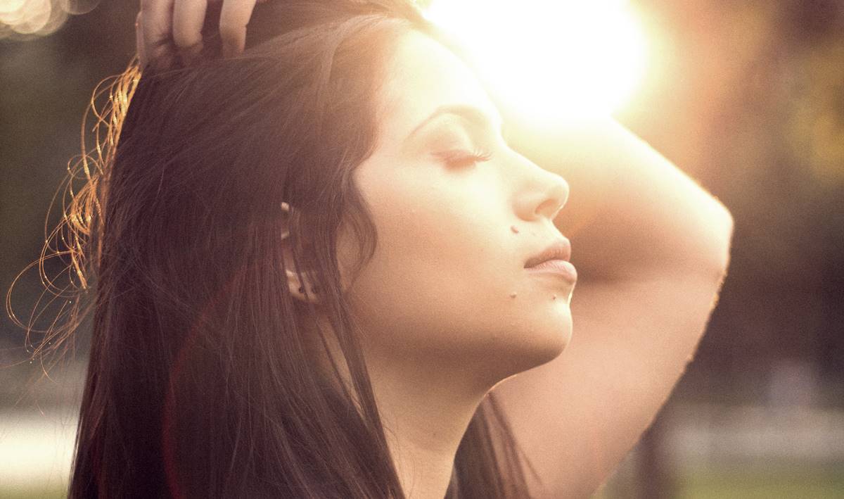 Fille aux yeux fermés devant le soleil se demandant pourquoi soupirons-nous ?