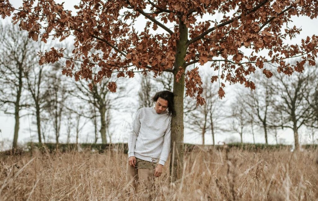 Chico apoyado en árbol pensando que me siento infravalorado por los demás