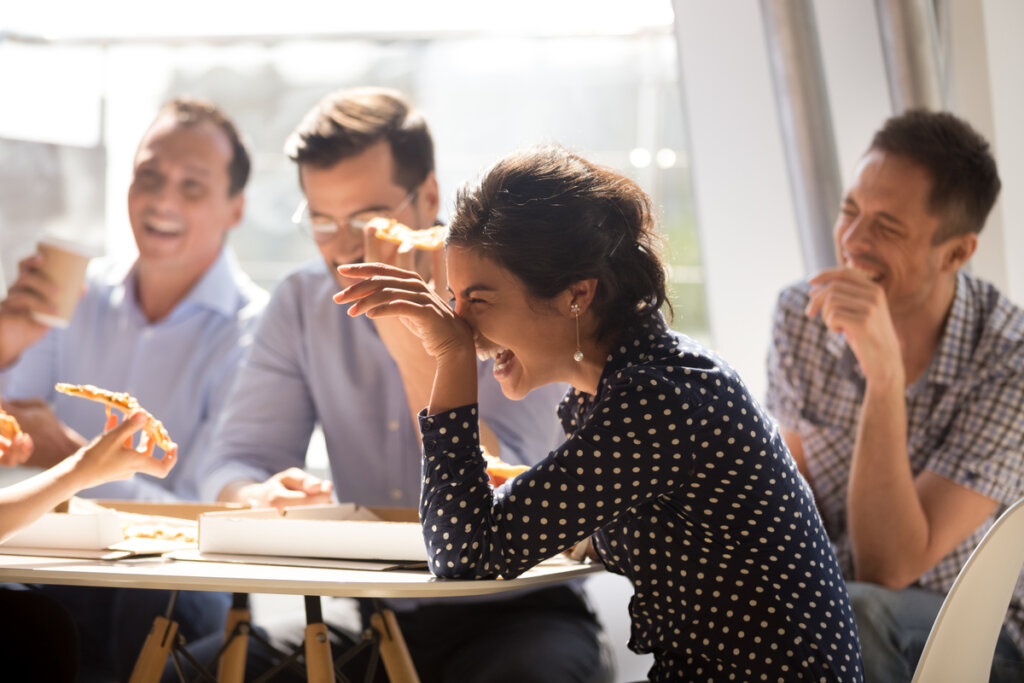 Friends laughing while sitting around a table and eating pizza.