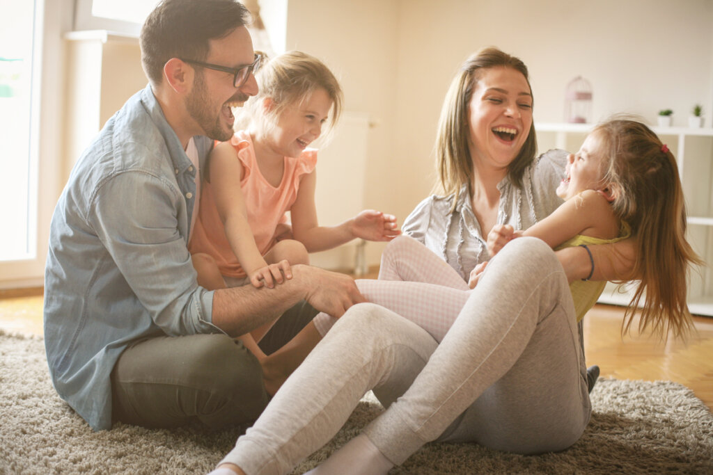 Parents sitting on the floor and laughing with their two young daughters.