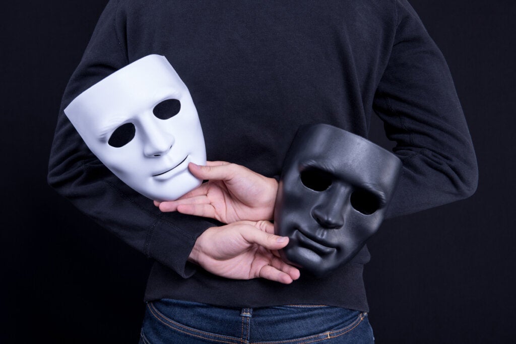 Hombre ocultando dos máscaras como gesto de hipocresía