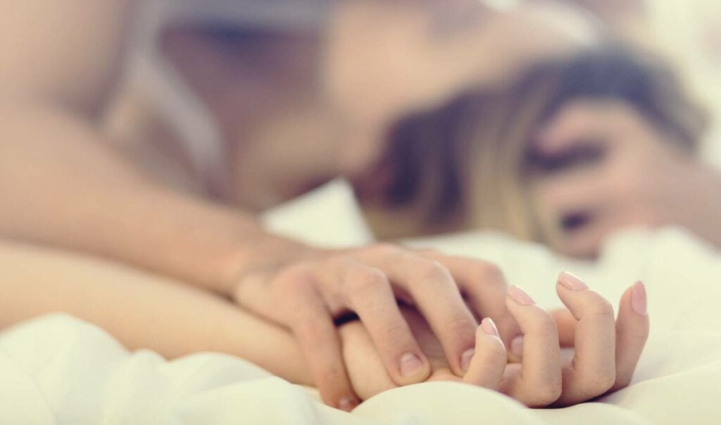 Mãos entrelaçadas de um casal na cama
