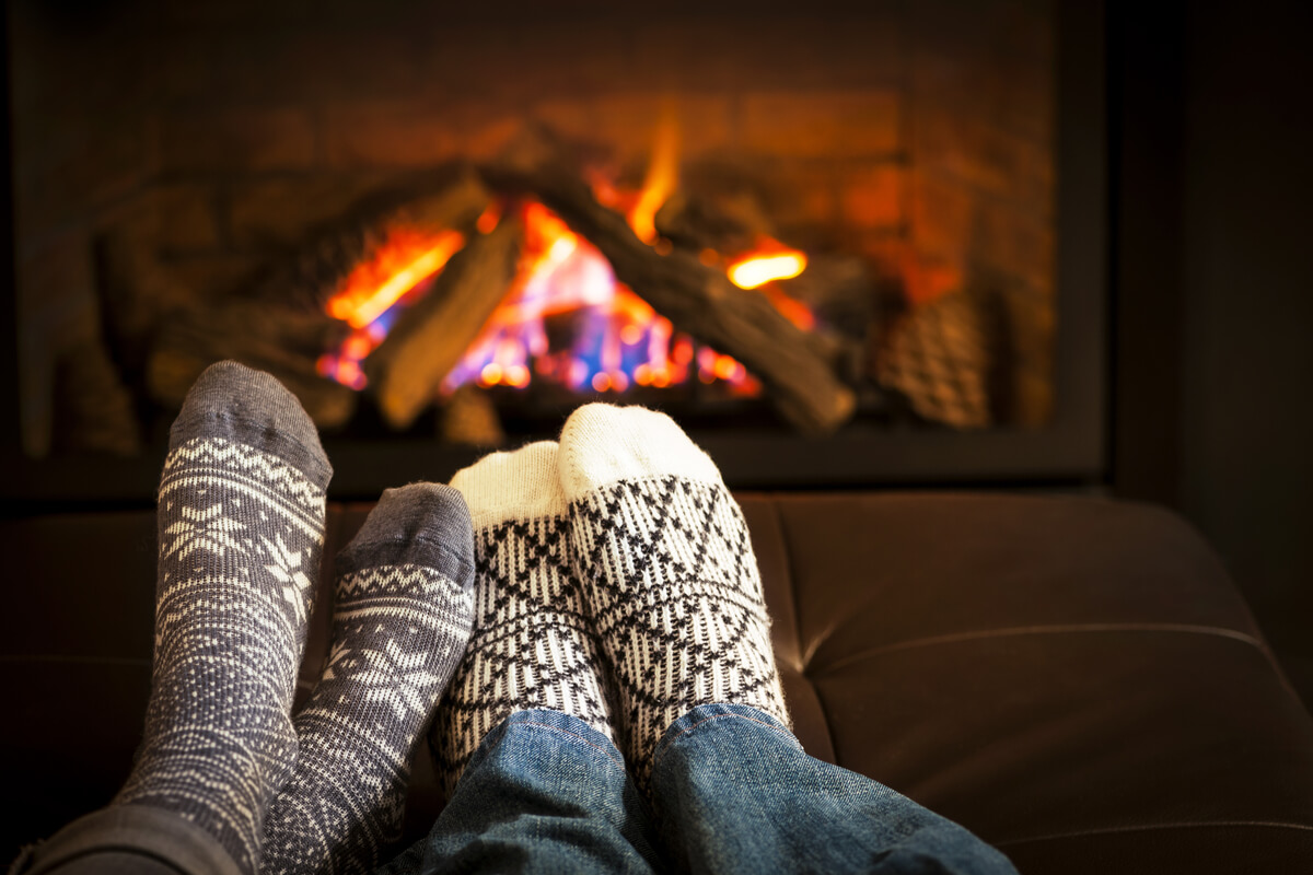 Pies con calcetines de una pareja frente a la chimenea practicando el cuffin season