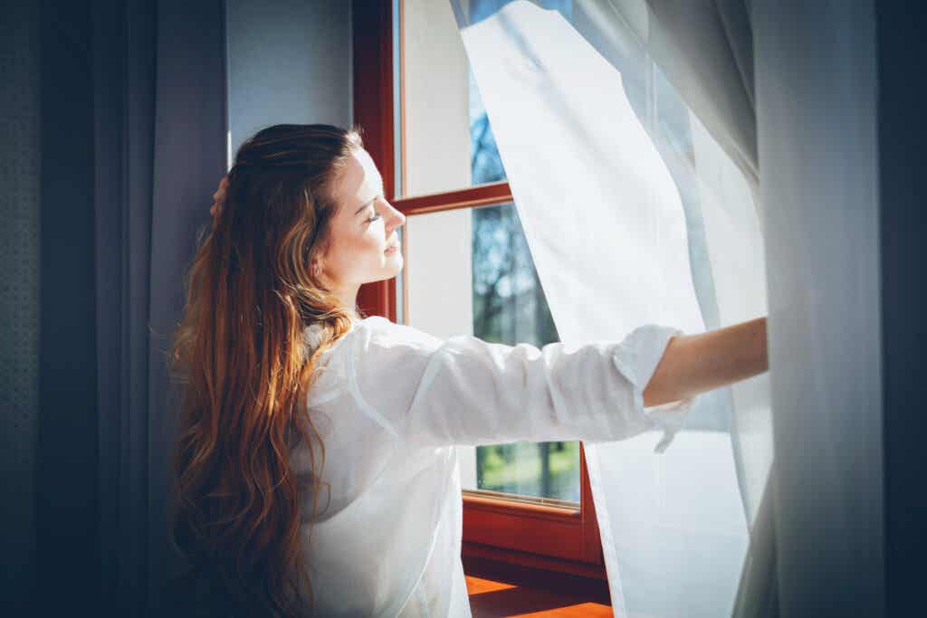 Mujer abriendo una ventana para disfrutar de la luz azul