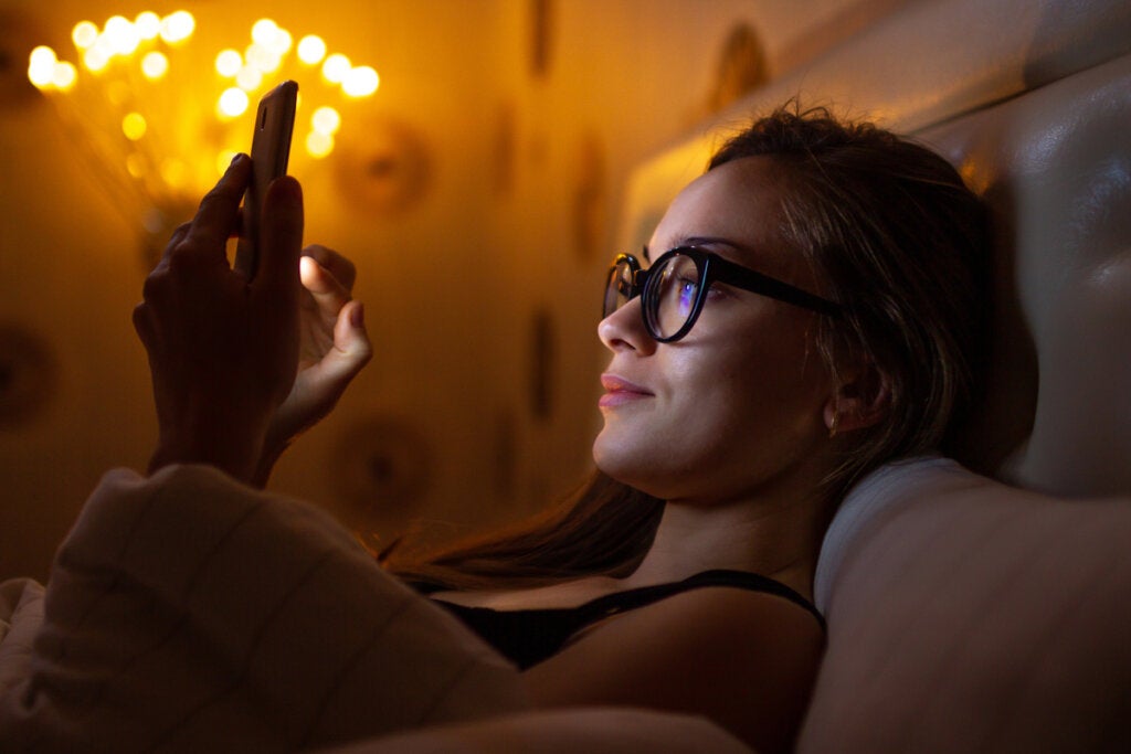 Vrouw in bed die naar mobiel kijkt die de impact tussen kunstmatig nachtlicht en depressie voorstelt