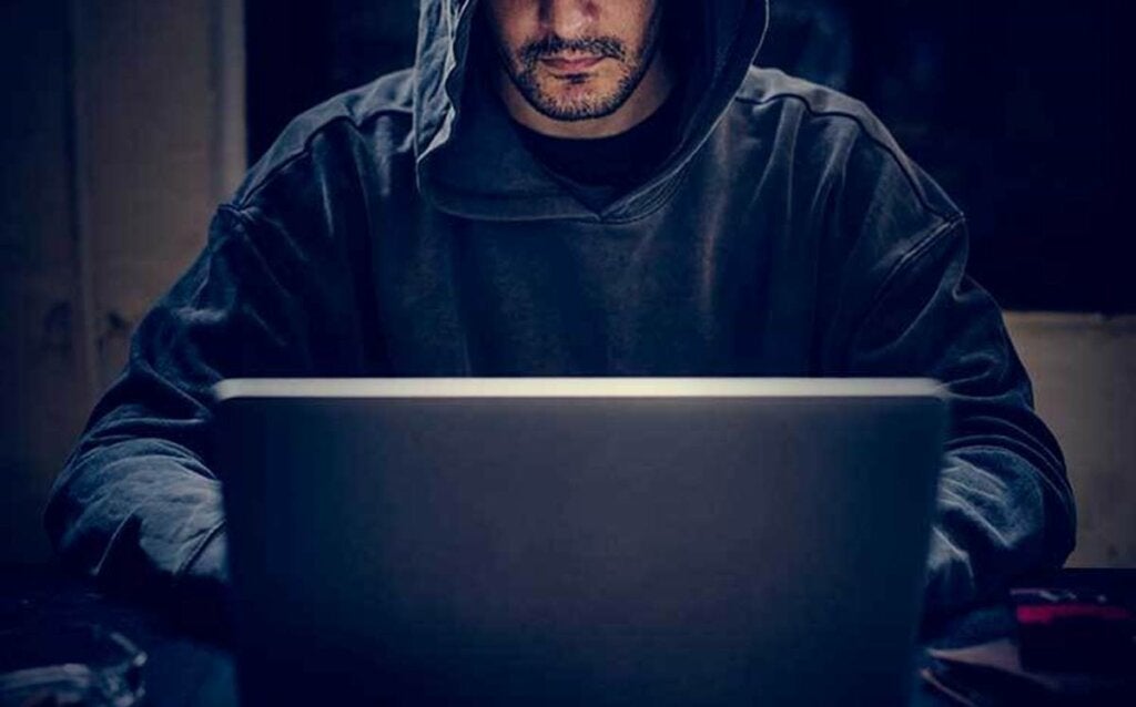 Hooded man at computer looking for how to recognize "dark triad" personality