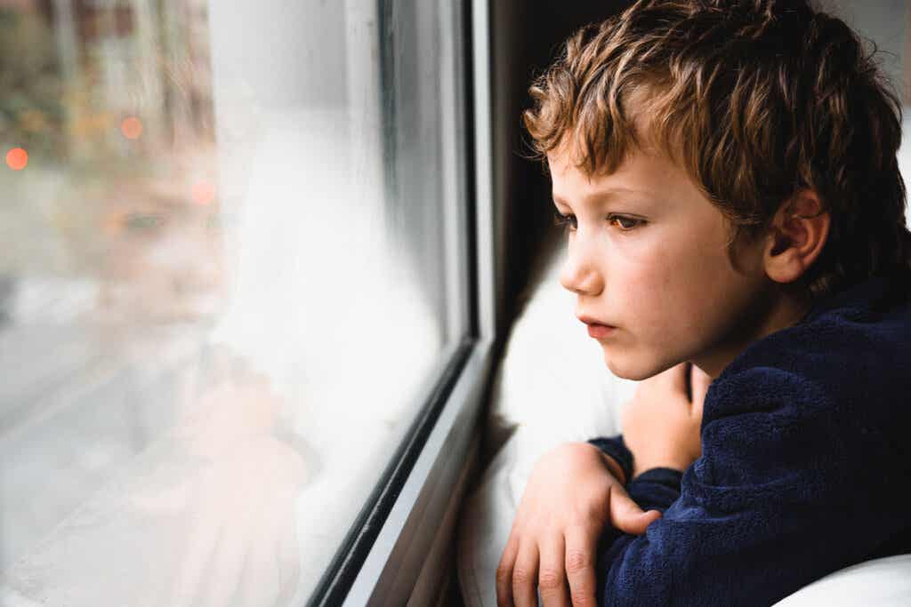 Niño triste mirando por la ventana para representar cómo el trauma infantil aparece en los escáneres cerebrales