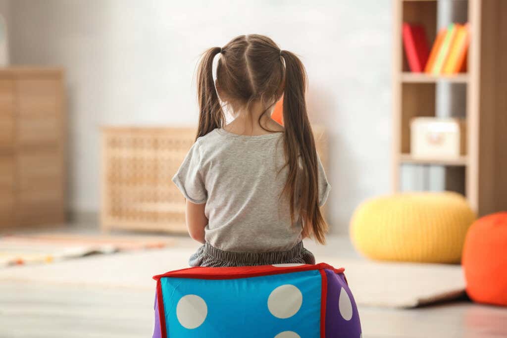 Dziewczyna odwrócona plecami siedzi na krześle w kształcie kostki