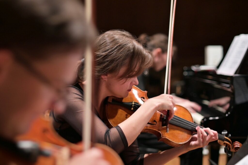 músicos tocando violines y, al fondo, un piano de cola.