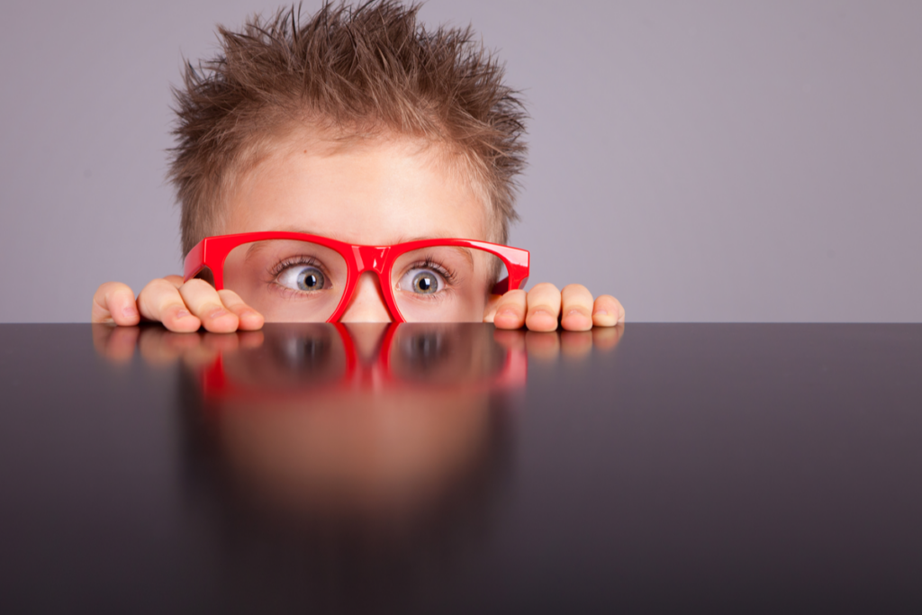 Curious child with red glasses symbolizing that children perceive stimuli that adults do not see