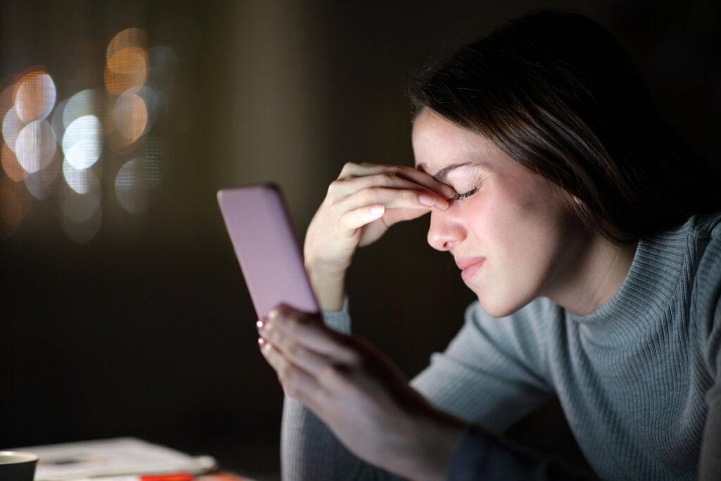 Stressed woman and cellphone, showing link between artificial light and depression.