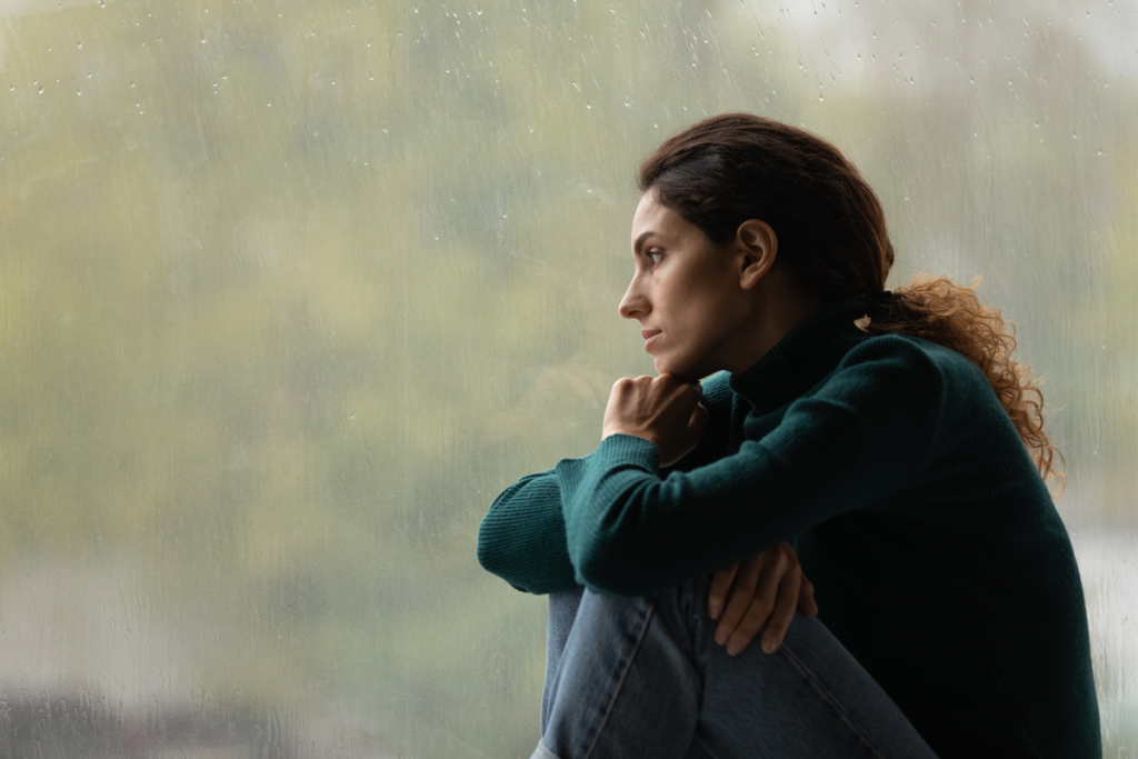 Worried woman looking out a window and applying the spiral of silence