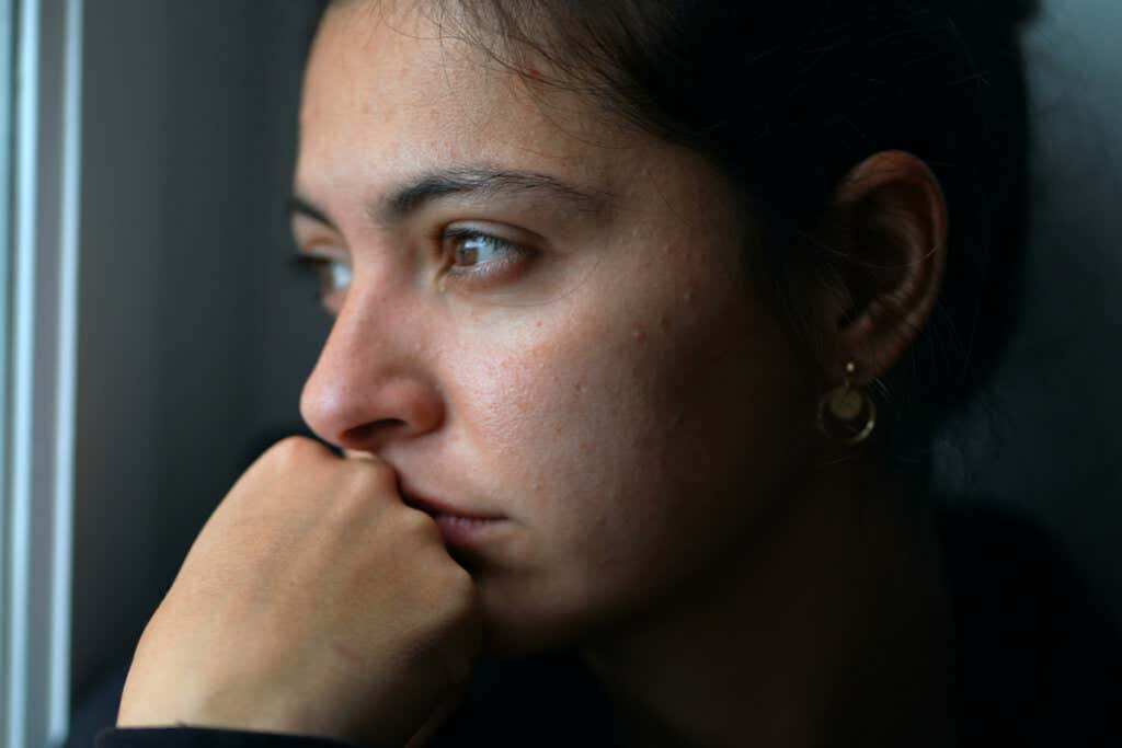 A woman looking out the window thinking with a sad look on her face.