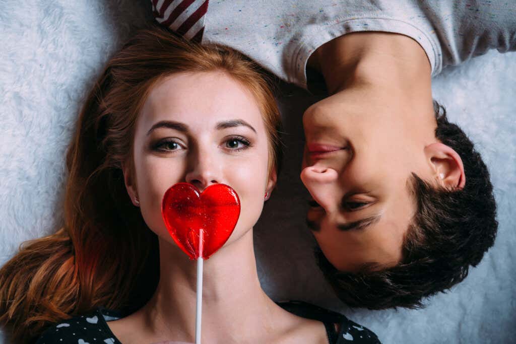 Couple lying with a heart lollipop symbolizing that if you are curious you will be happy