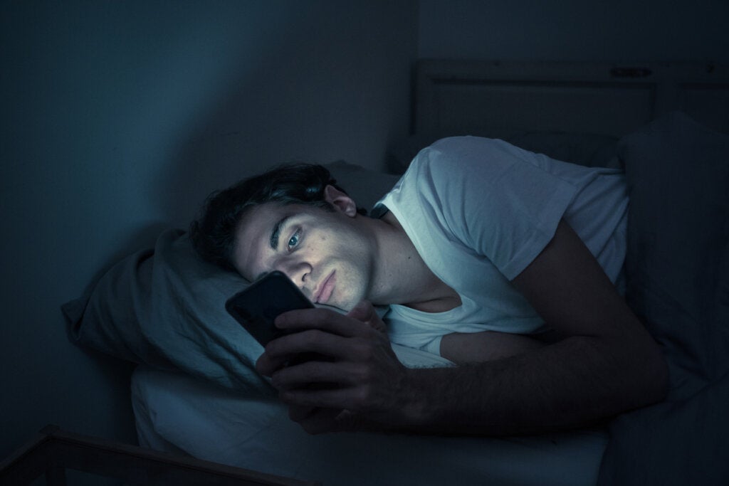Ragazzo che guarda il cellulare di notte che rappresenta il collegamento tra l'auto-domanda e i social network