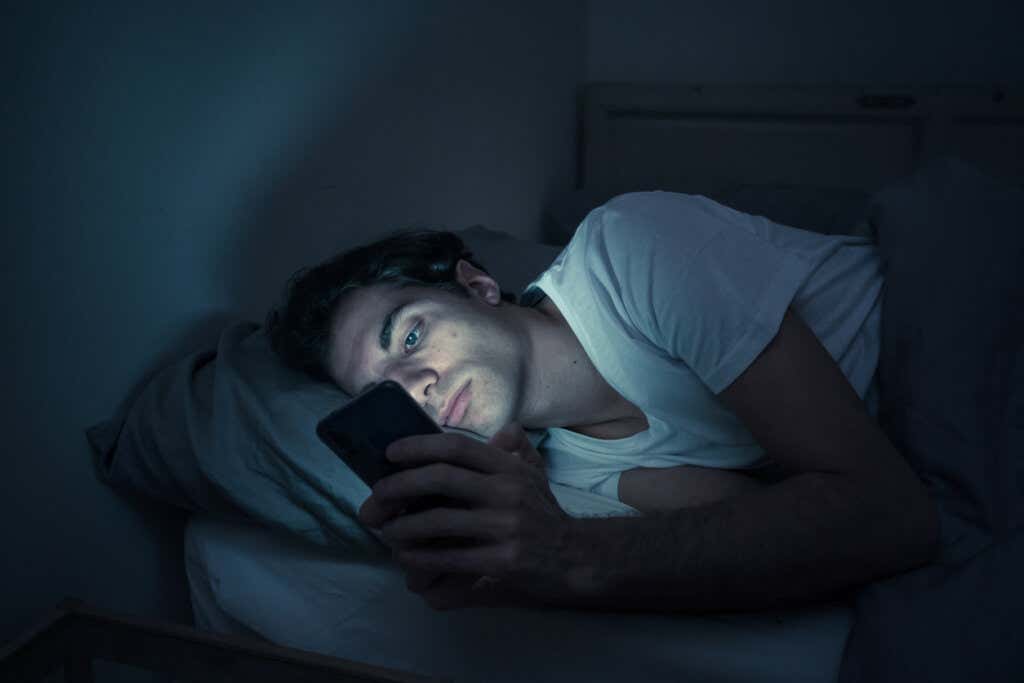Garçon regardant le mobile la nuit représentant le lien de l'auto-demande et des réseaux sociaux