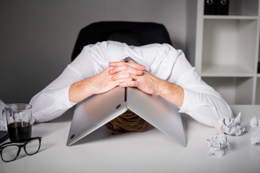 Mies piiloutuu kannettavan tietokoneensa alle työstressin vuoksi.