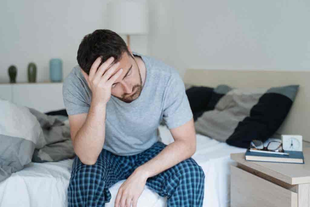 Un hombre que está sentado en cama sufre trastorno del sueño