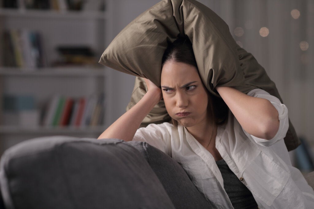 Angry woman covering her head with a cushion symbolizing Why are we in a bad mood when we are hungry?