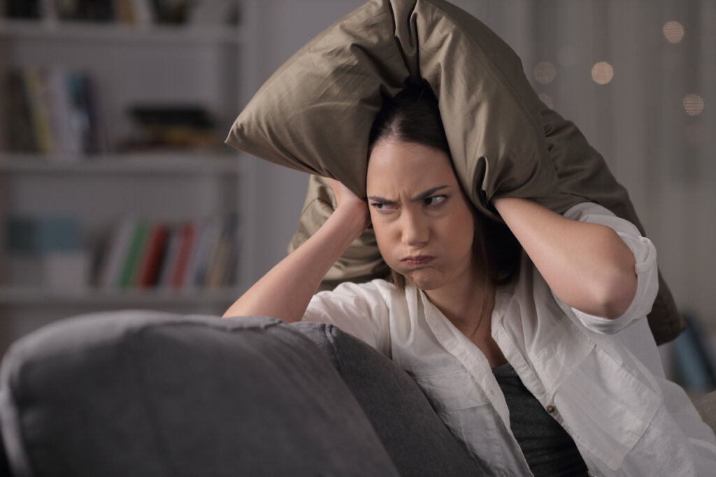 Mulher irritada cobrindo a cabeça com uma almofada simbolizando Por que estamos de mau humor quando estamos com fome?