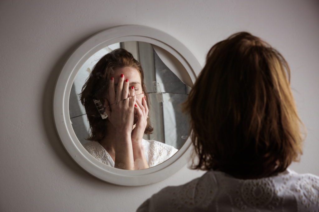 Woman covering her face in front of a mirror