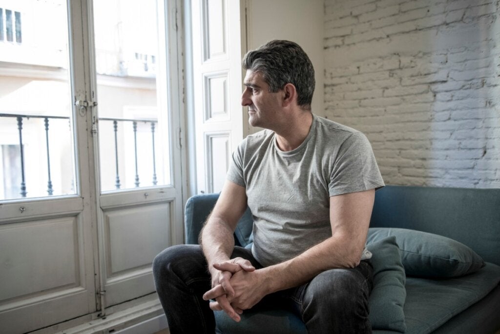 Een trieste man kijkt zittend in de woonkamer naar het balkon van zijn huis