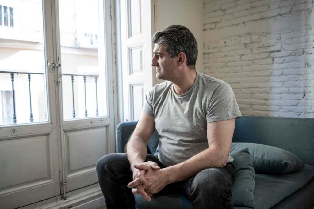 Un uomo triste guarda seduto in soggiorno dal balcone di casa sua.