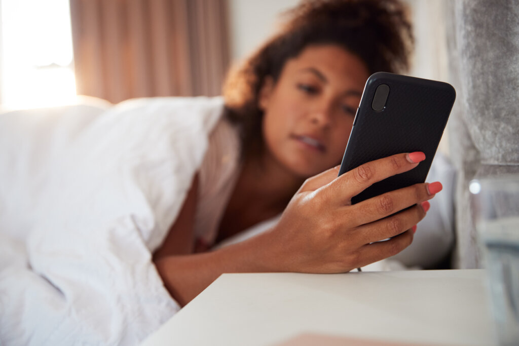 Mulher olhando para o celular ao acordar