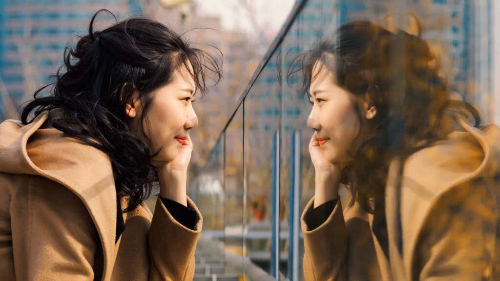 An Asian woman on a bridge looking at her reflection in the glass railing.
