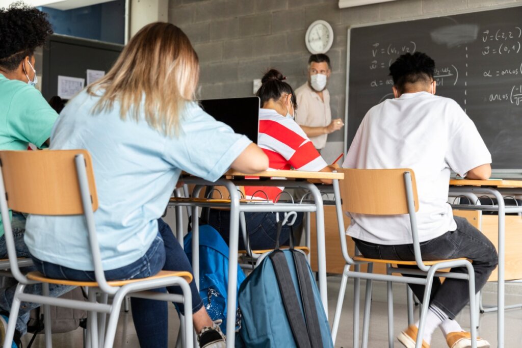 Nauczyciel z maską na twarz przedstawia lekcję matematyki uczniom szkół średnich