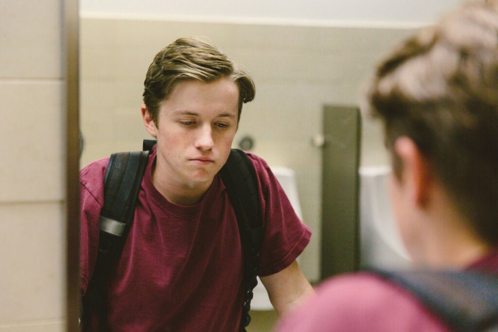 Trist tenåring som ser seg i speilet og tenker at han lider av tomt hjertesyke