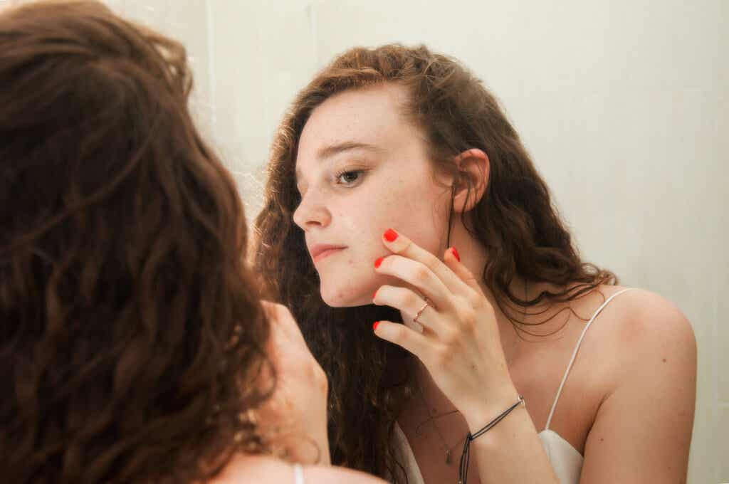 Tenåring ser på ansiktet hennes med akne i speilet.