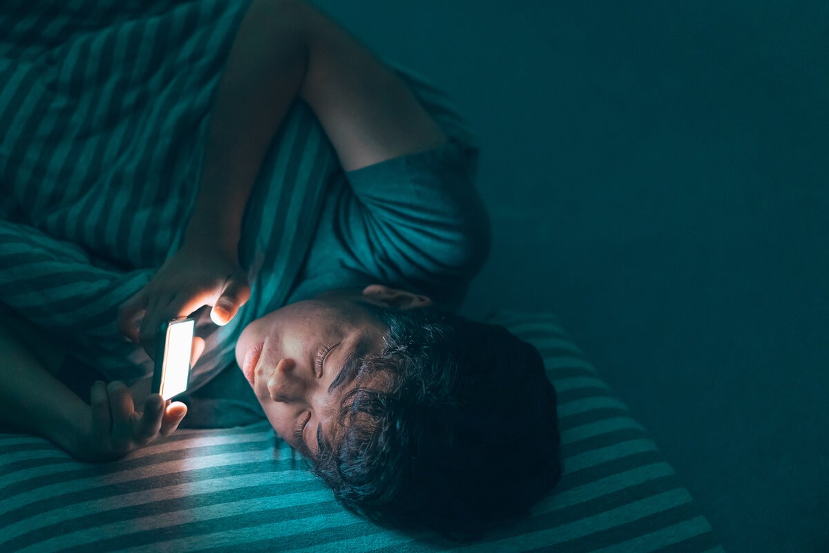 Tiener in bed op zijn mobiel