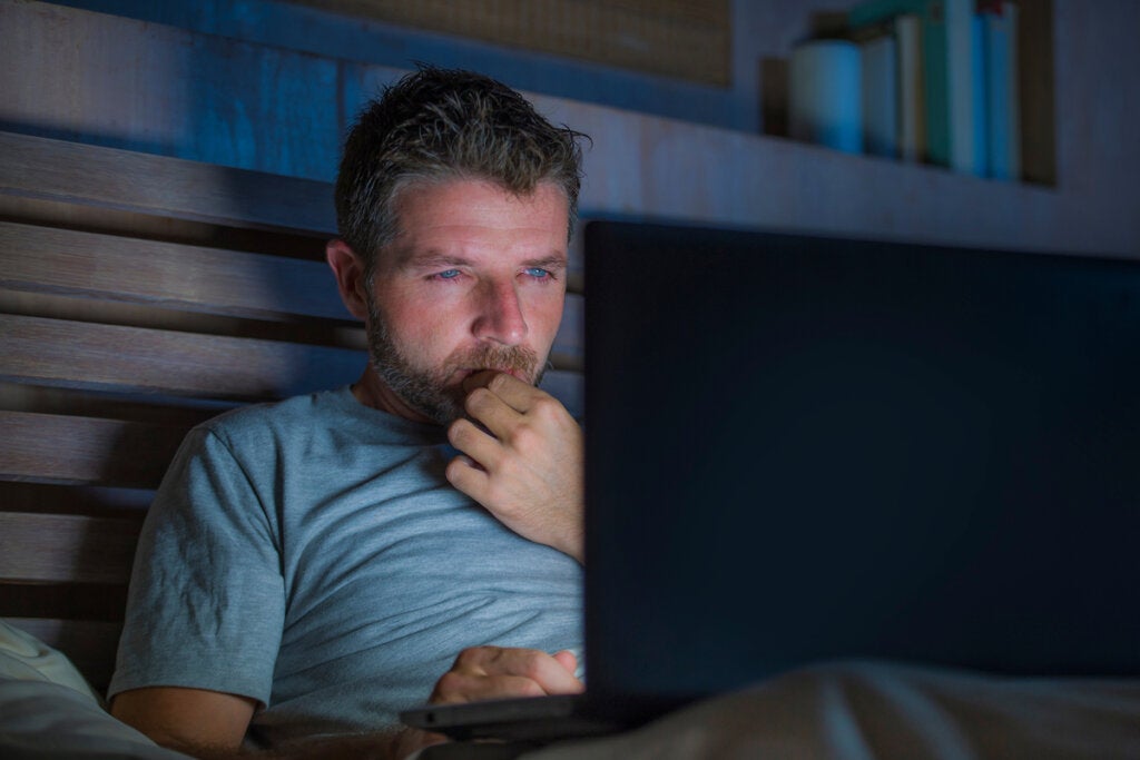 Mężczyzna ogląda porno na komputerze w swoim łóżku