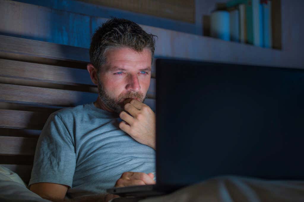 Homem assistindo pornografia no computador em sua cama