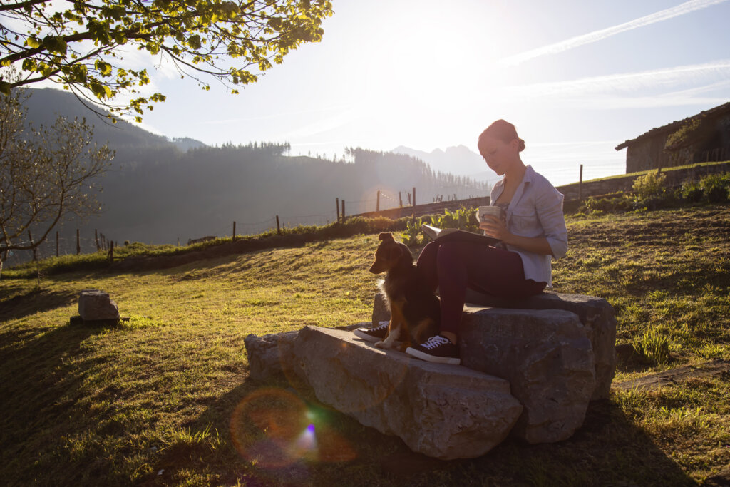 Mujer joven leyendo libros de psicología positiva a la luz del amanecer en compañía de su perro.