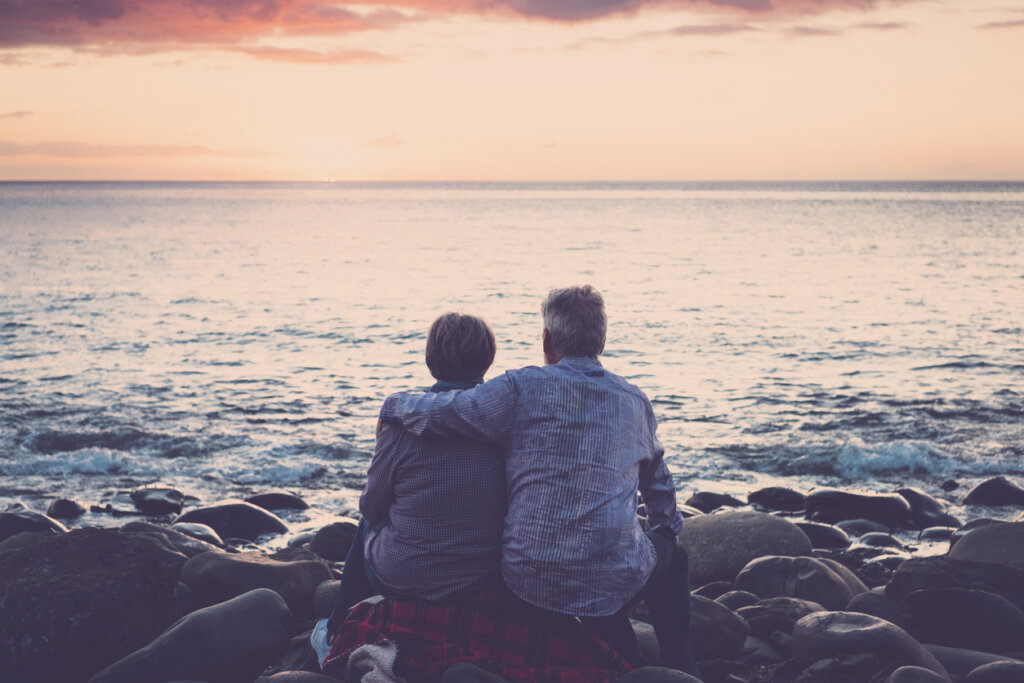 Elderly couple sitting and hugging each other in the sea at sunset. thinking about the myth of soul mates