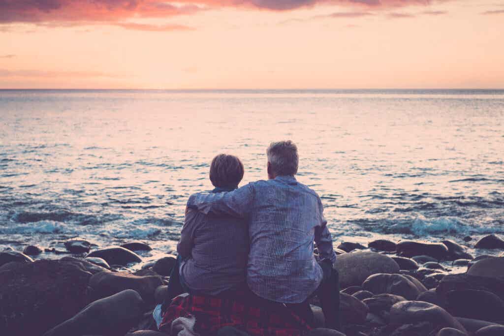 Eldre ektepar sitter og klemmer hverandre i sjøen ved solnedgang. tenker på myten om sjelevenner