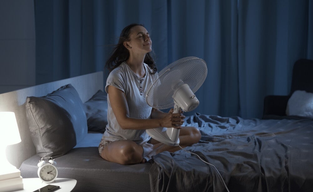 Woman turns on fan to sleep in the heat.