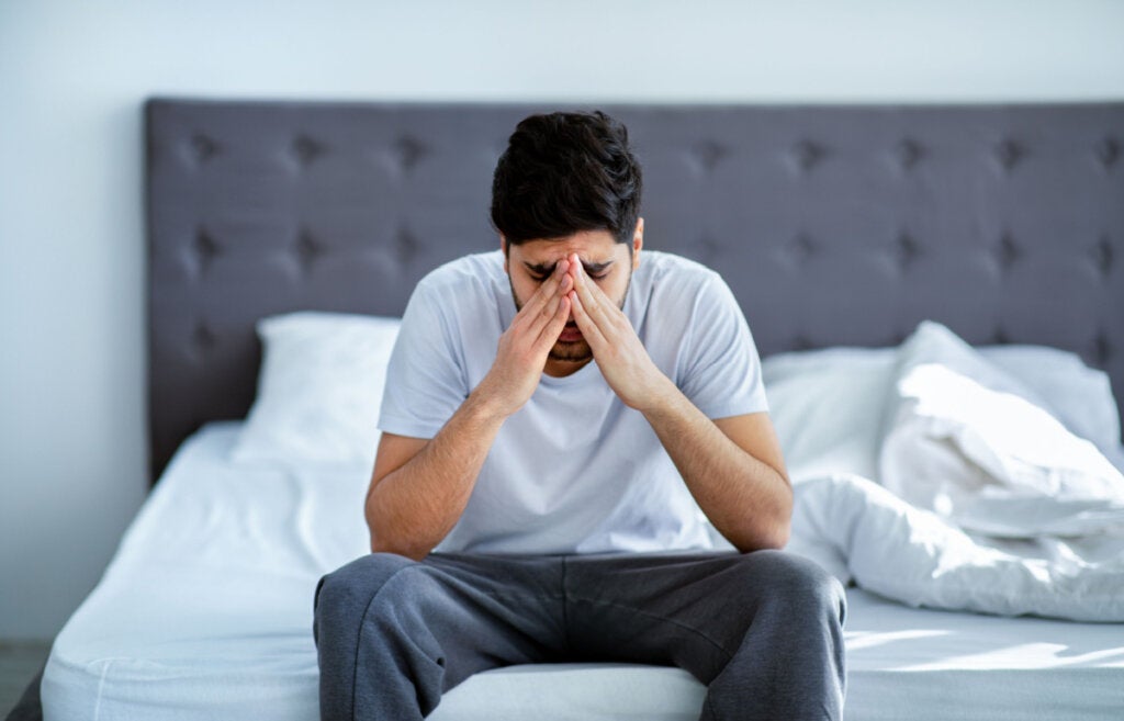 Sad man sitting in bed suffering paranoia and schizophrenia