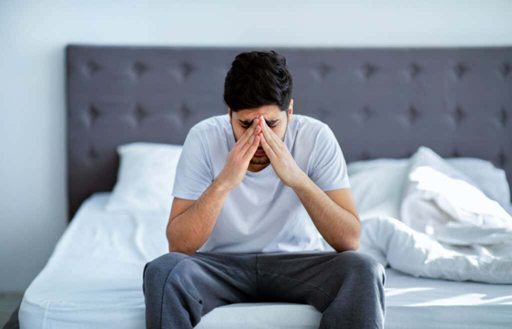 Triste uomo seduto a letto che soffre di paranoia e schizofrenia