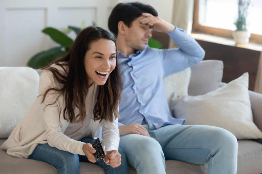Mujer riéndose viendo la tele con un hombre aburrido