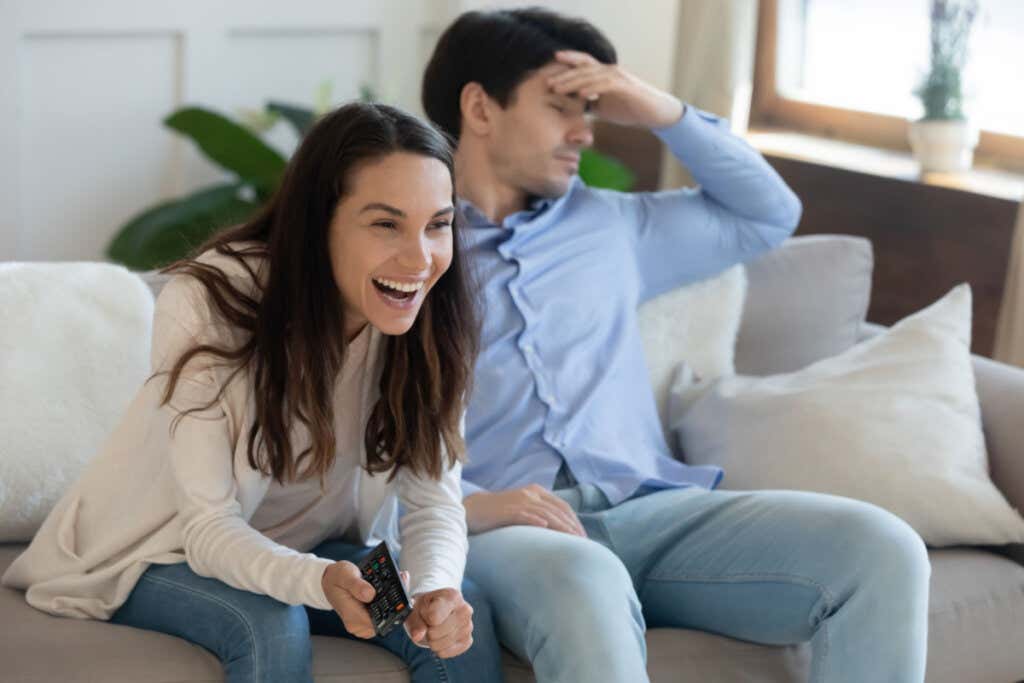 Mulher rindo assistindo tv com homem entediado